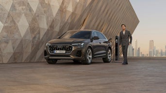 The Q8 SUV is parked at an angle in front of a modern building. A hedge separates the vehicle from the fully glazed building behind it.