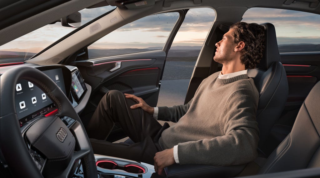 View through the driver's-side window of a young man sitting in the front passenger seat of the A6 Saloon with the door open.