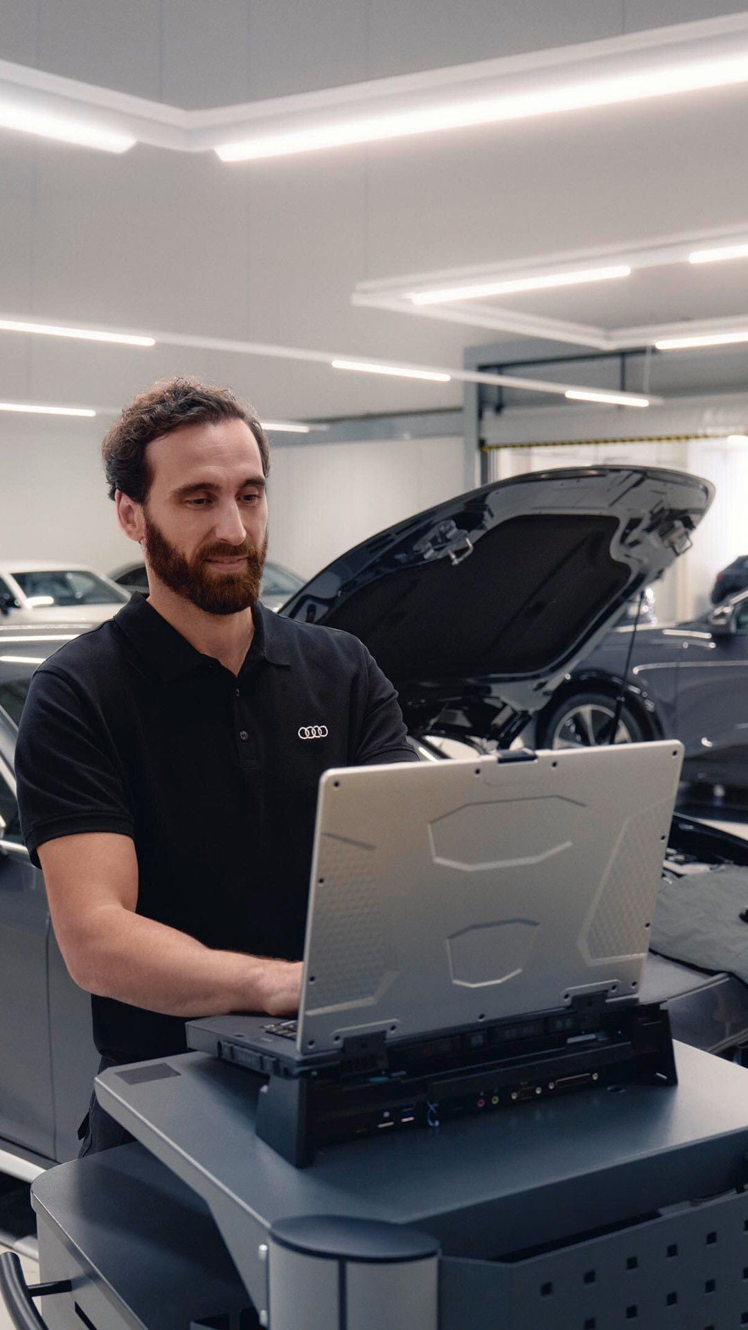 Zwei Mitarbeiter prüfen in der Werkstatt ein Auto mit geöffneter Motorhaube und Diagnosegerät.