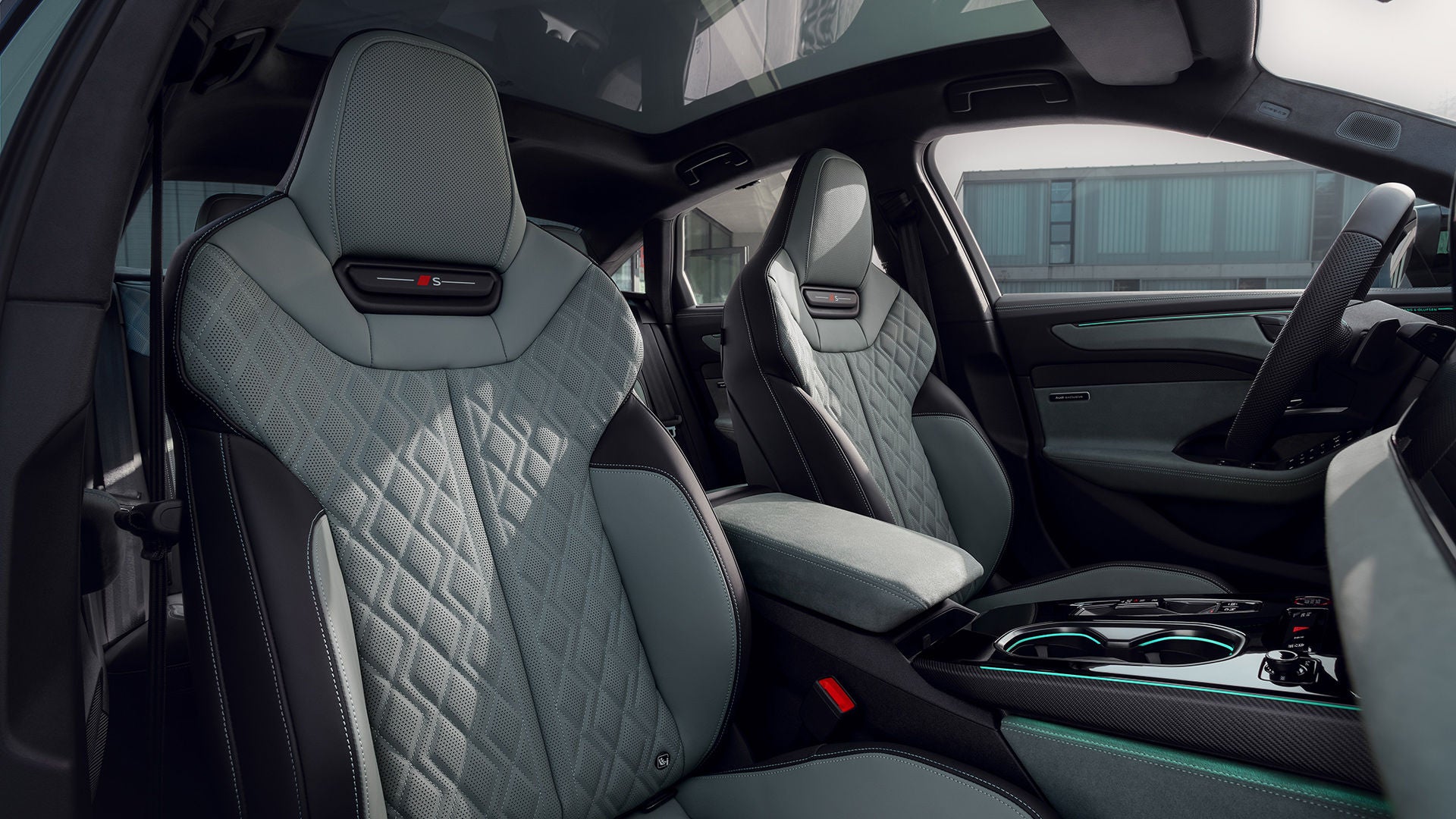 Interior of an Audi A6 sedan with two gray-green sports seats, center console, and large glass roof; subtle ambient lighting.