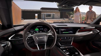 Ein Frau und eine Mann gehen auf einen Audi zu, im Vordergrund sieht man das Interior des Fahrzeugs.