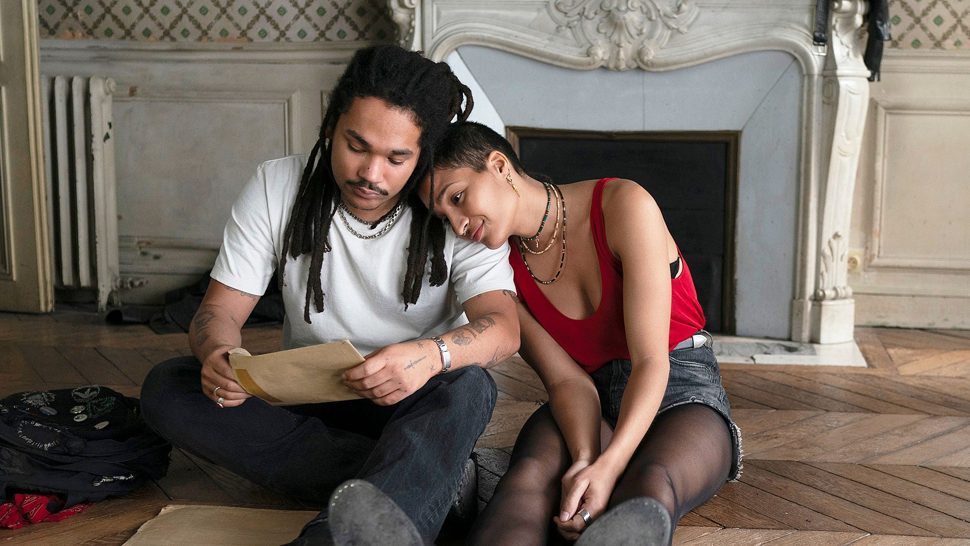 Bruder und Schwester sitzen am Boden und öffnen einen Briefumschlag.