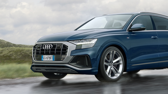 Inquadratura anteriore di un veicolo Audi in movimento su una strada bagnata, con dettaglio sui pneumatici.