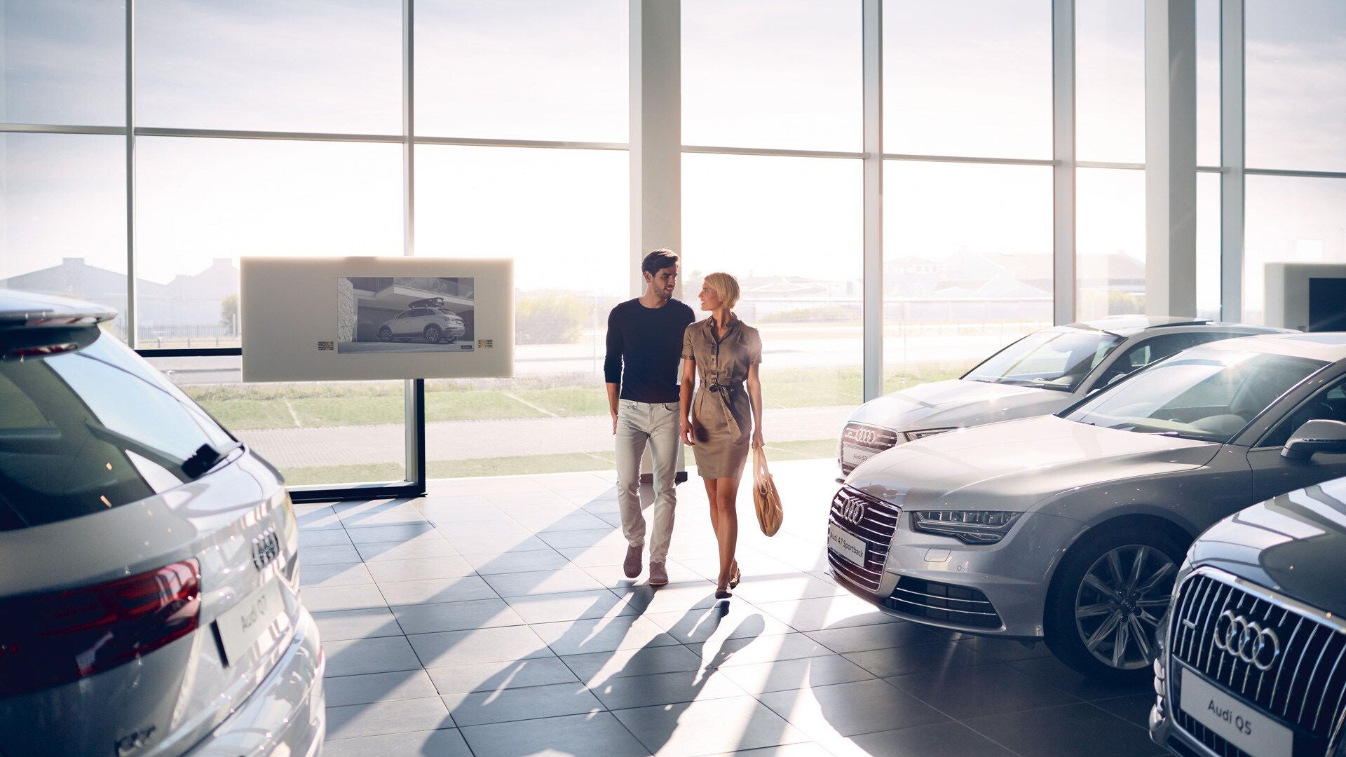 Ein Mann und eine Frau laufen nebeneinander durch ein Audi Autohaus und lächeln einander an.