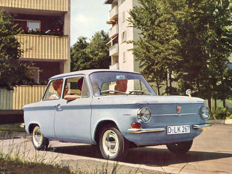 Coloured photo of several people in a light blue NSU Prinz in front of residential buildings 