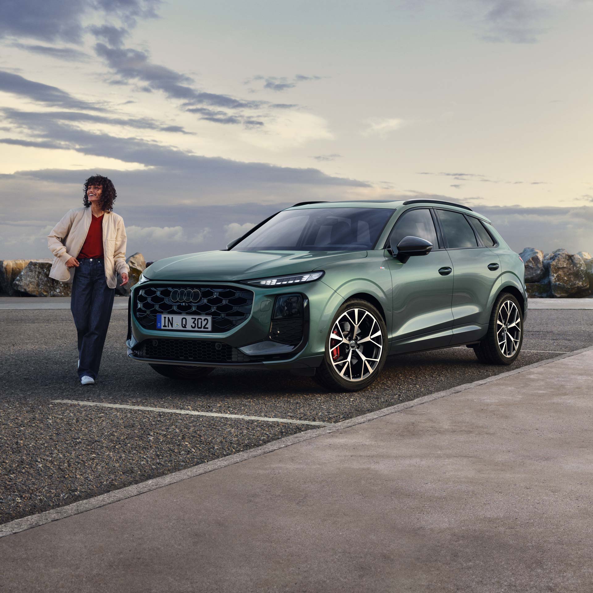 Audi Q3 står på en parkeringsplats, en person lutar sig mot bilen. 