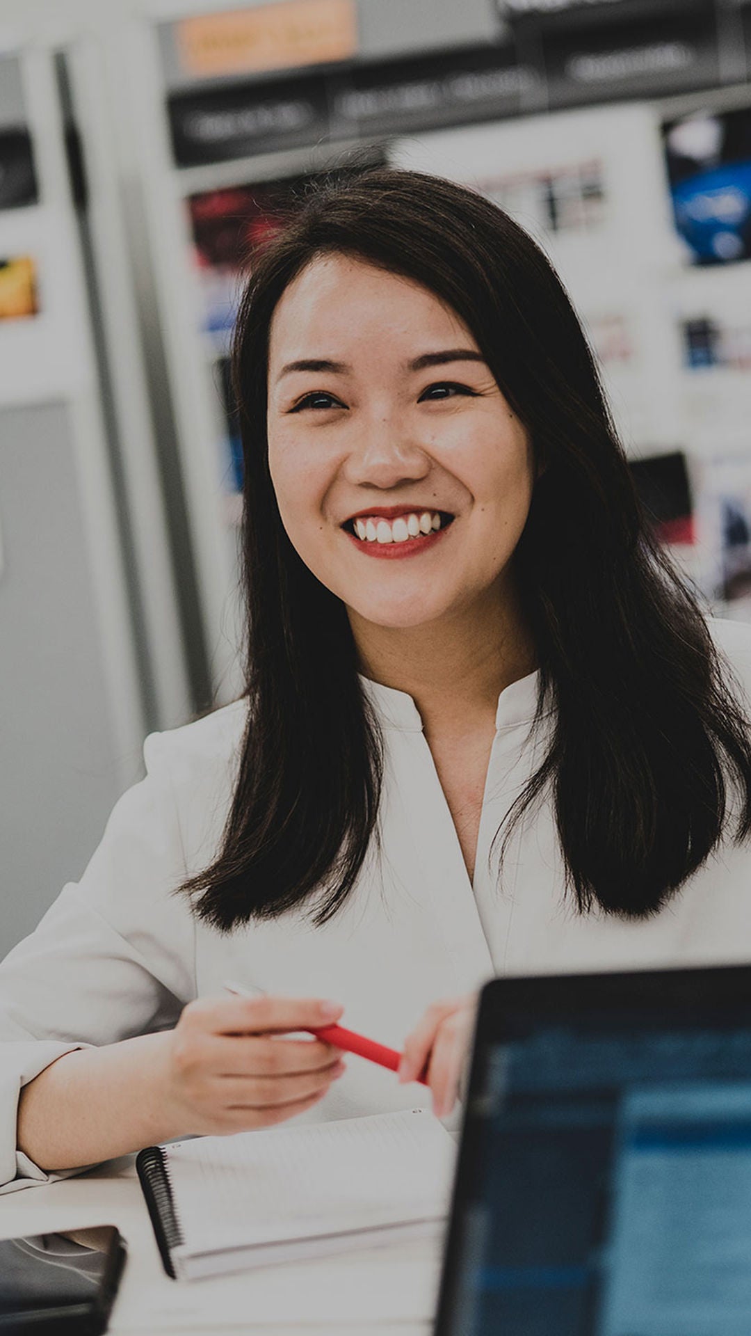 A woman sits at a table with a laptop in front of her and laughs past the camera