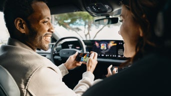 Zwei Personen spielen ein digitales Kartenspiel in einem Audi, angezeigt auf Smartphones und dem zentralen Bildschirm.