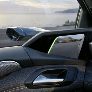 Nahaufnahme des virtuellen Außenspiegels des Fahrers und dem OLED-Display, welches die Kamerasicht anzeigt. Im Hintergrund ist das Meer zu sehen.