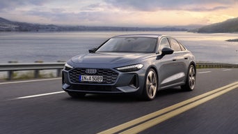 Die A5 Limousine im schrägen Frontprofil. Das Fahrzeug fährt auf einer Straße entlang der Küste. Im Hintergrund beginnt die Dämmerung.