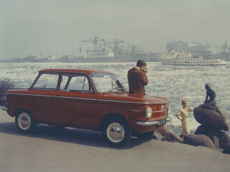 A man takes a photo of a woman in front of the Little Mermaid in Copenhagen, leaning against a red NSU Prinz