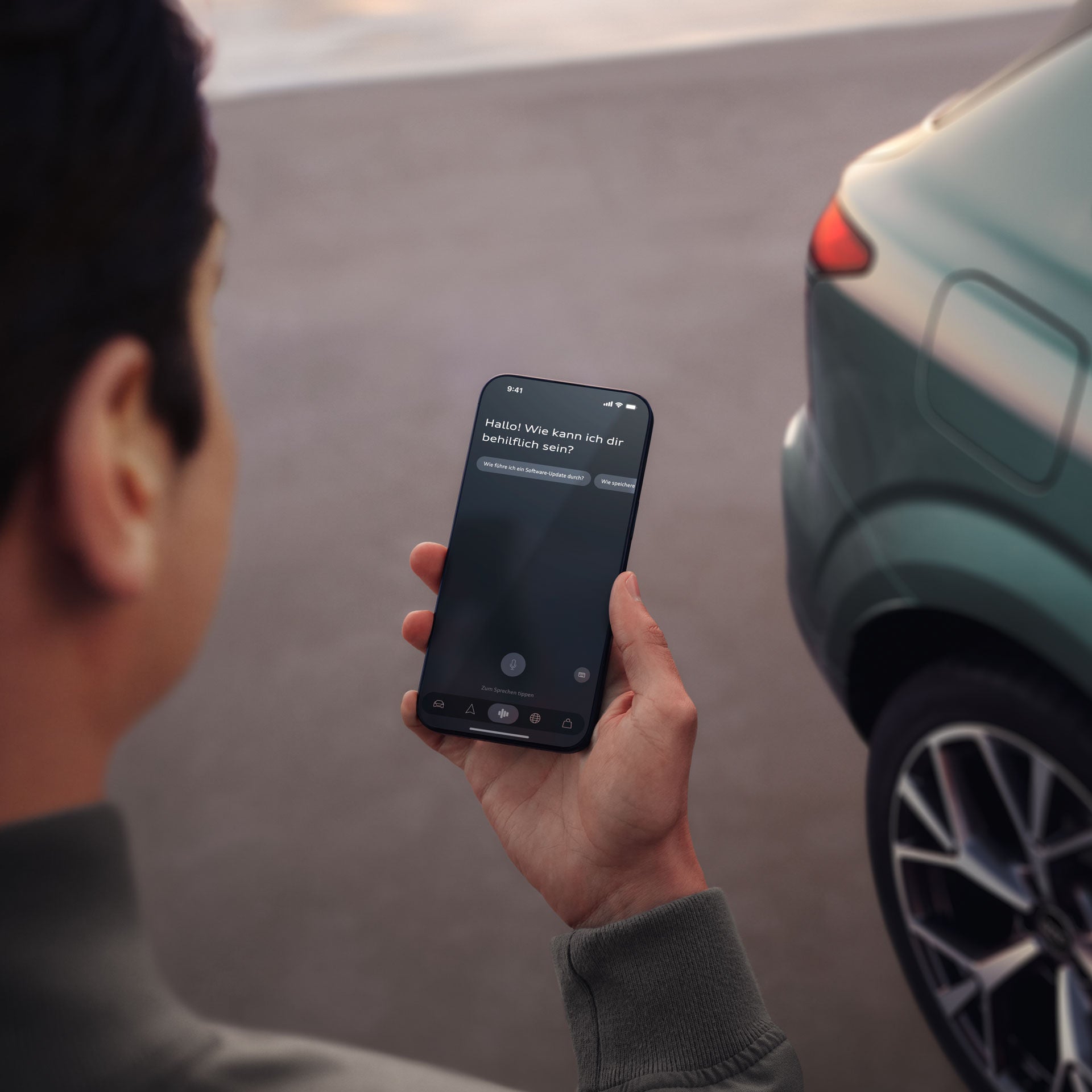 Mann schaut auf einen Bildschirm eines Handys und man sieht einen grünen Audi im Hintergrund