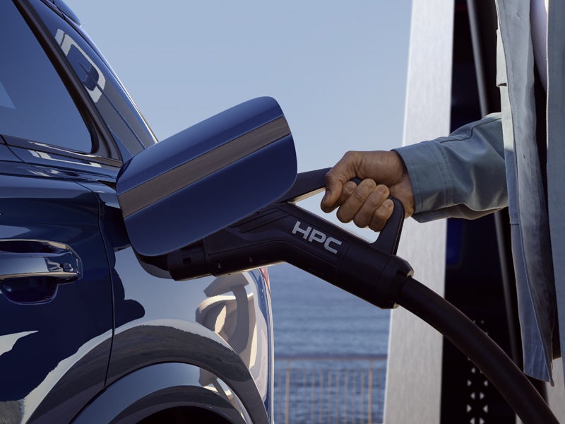 Nahaufnahme der Ladebuchse des SQ6 Sportback e-tron, in welche ein Mann gerade ein Ladekabel einsteckt.