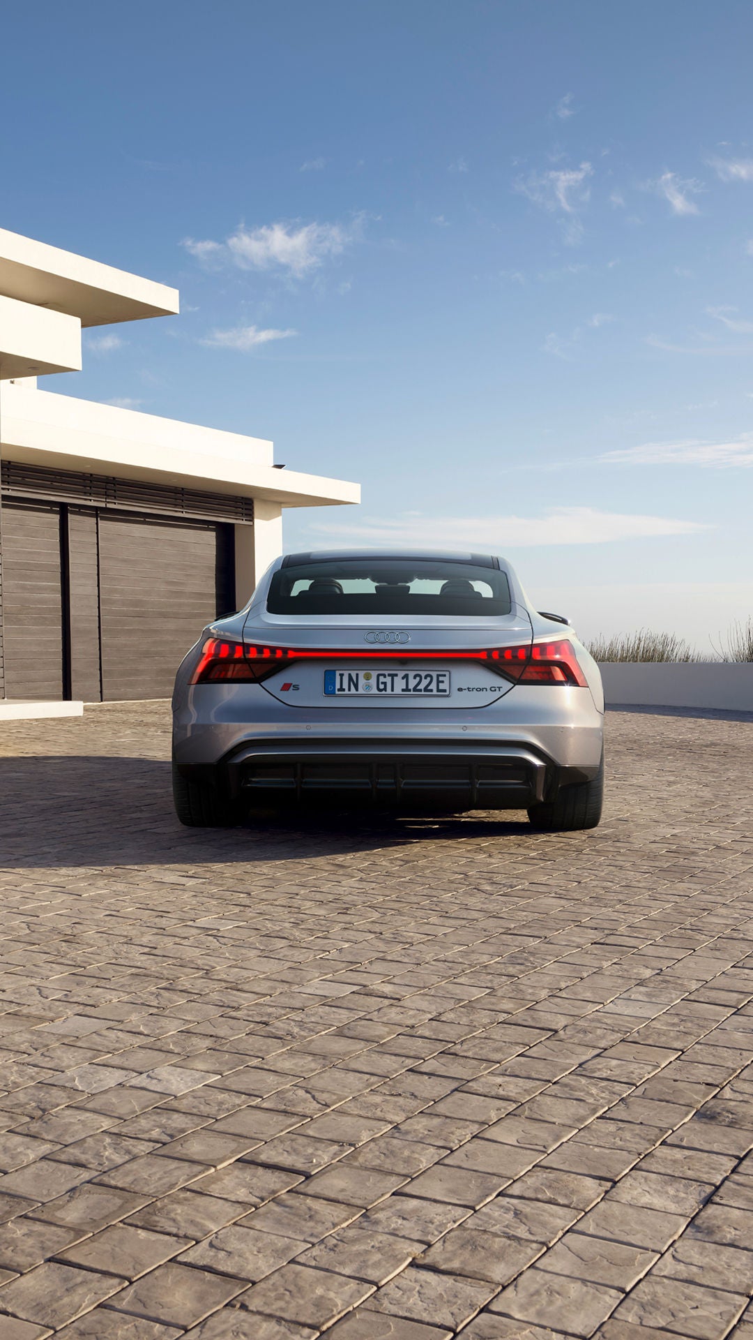 Silver Audi S-e-tron GT parked outside a modern house with a clear sky.
