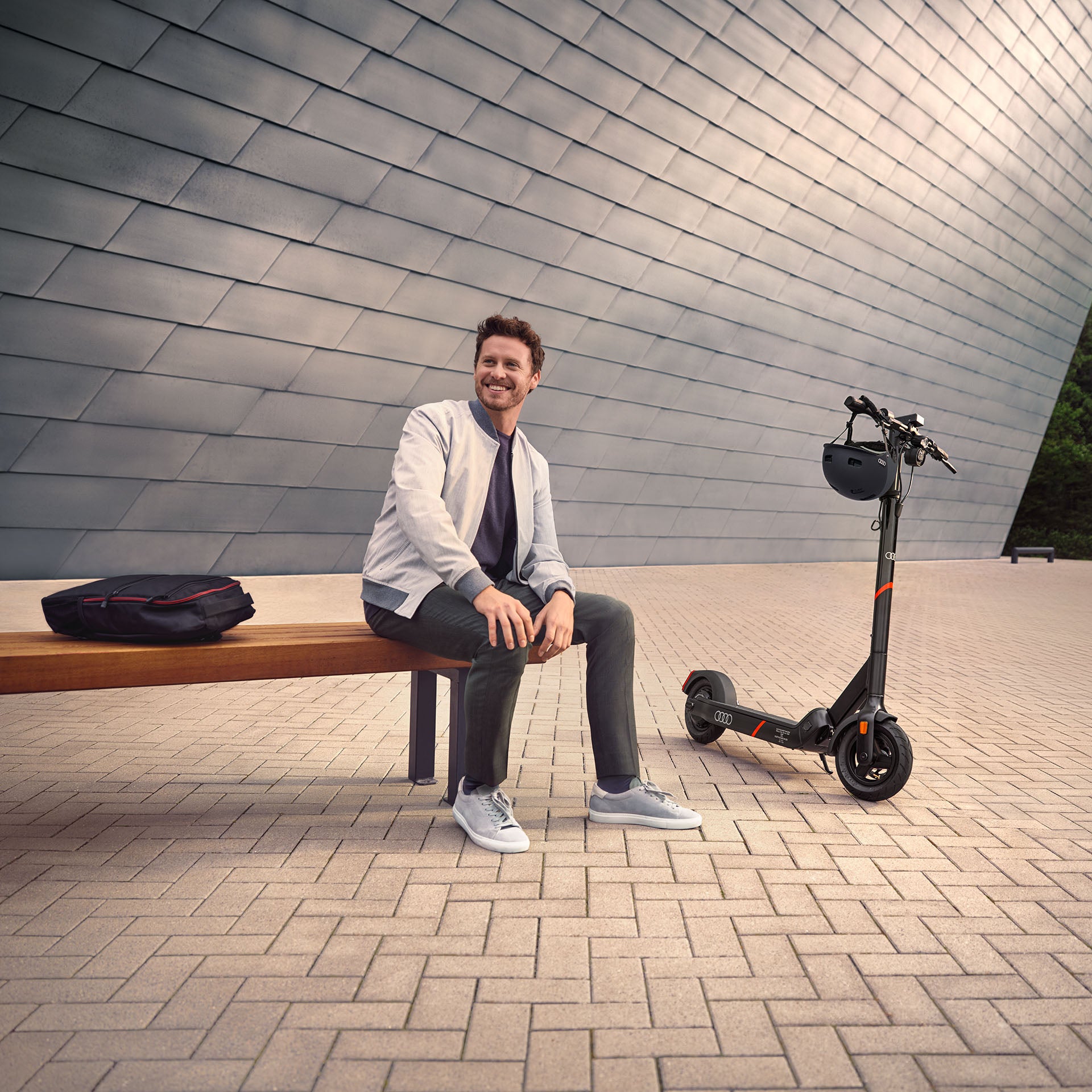Ein Mann sitzt auf einer Bank und neben ihm ist ein electric kick scooter von Audi