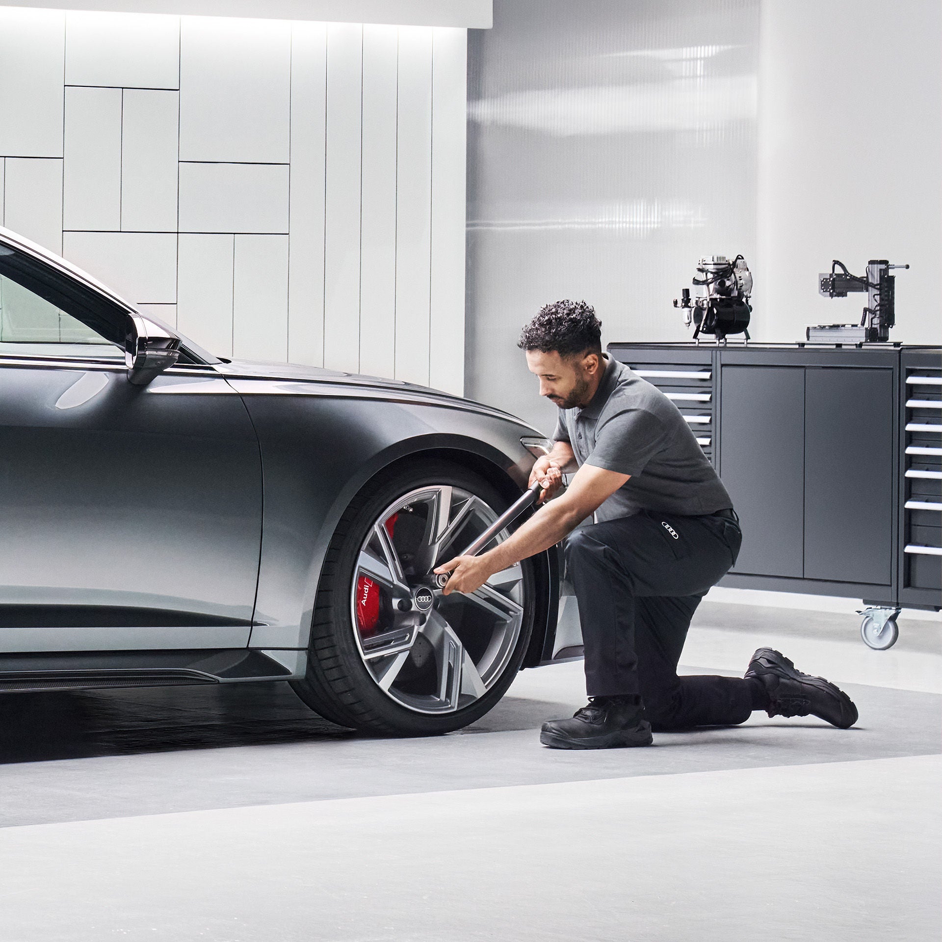 En man som byter fälgar på en mörkgrå Audi RS i en Audiverkstad
