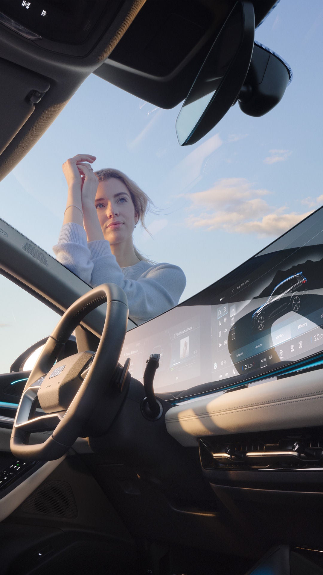 Blick über das MMI eines Audi, durch die Windschutzscheibe. Eine Frau lehnt am Auto und schaut in die Ferne.