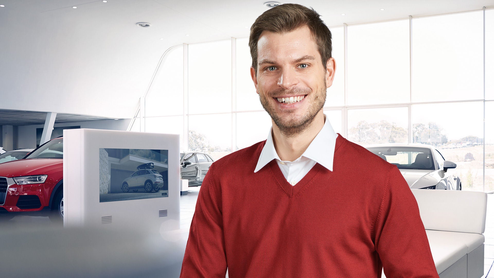 Audi Serviceberater steht im Autohaus und lächelt in die Kamera.
