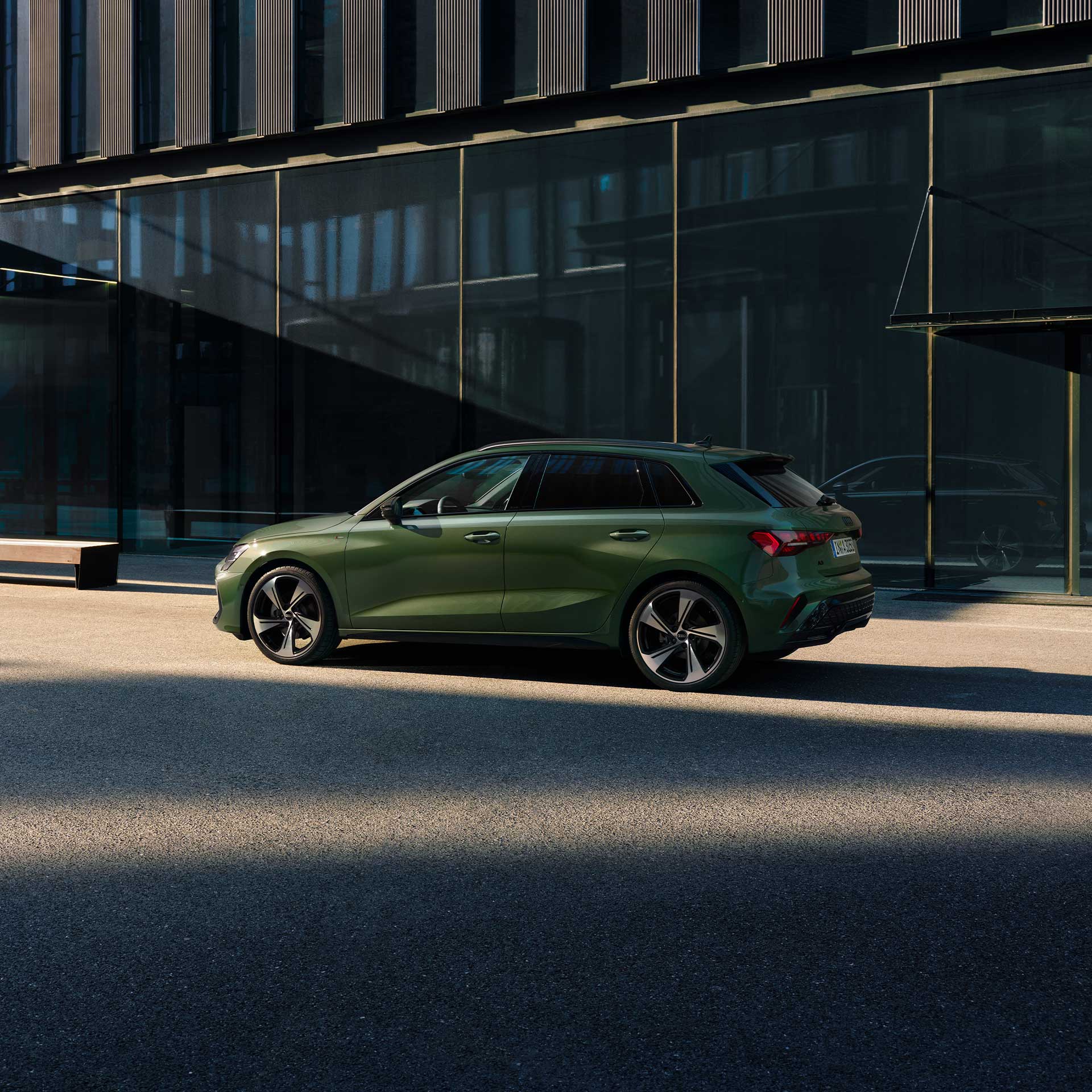 Grüner Audi A3 Sportback in Seitenansicht, geparkt auf einer Straße vor einem modernen Gebäude mit dunkler Glasfassade.