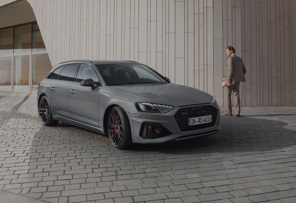 A grey car parked outside a modern building with textured walls.