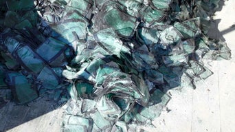 Haufen zerbrochener, grünlich schimmernder Glasscheiben auf einem hellen Betonboden.