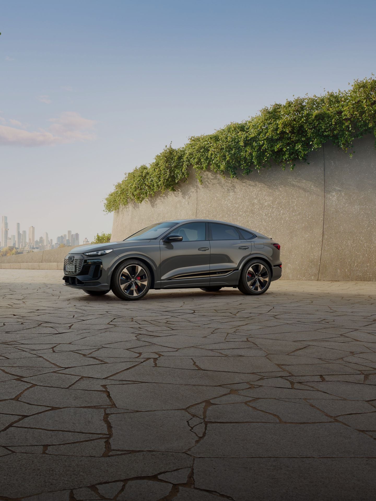 Audi Q6 Sportback e tron parked on a modern designed cracked patio with plants and city skyline in the background.