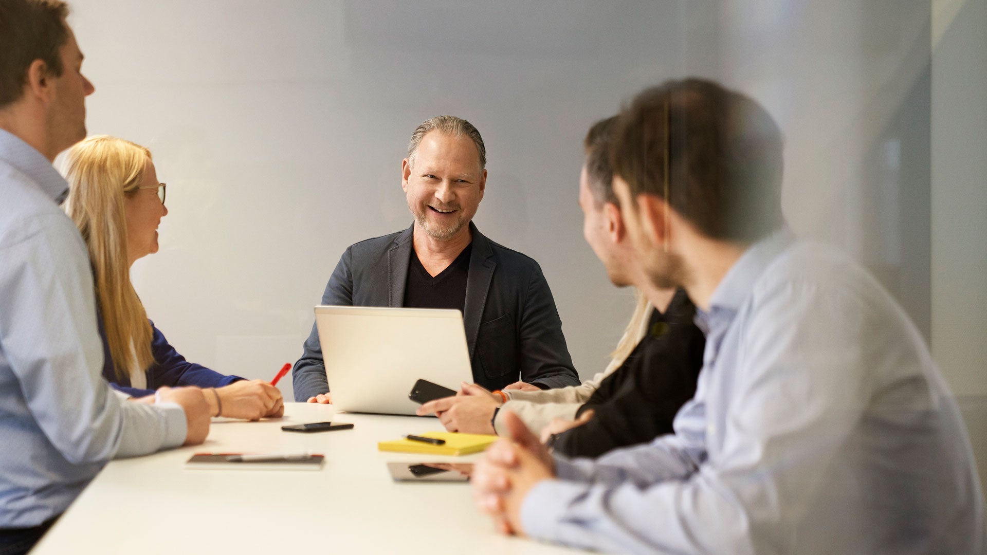 Fünf Mitarbeitende sitzen an einem Tisch und lachen miteinander