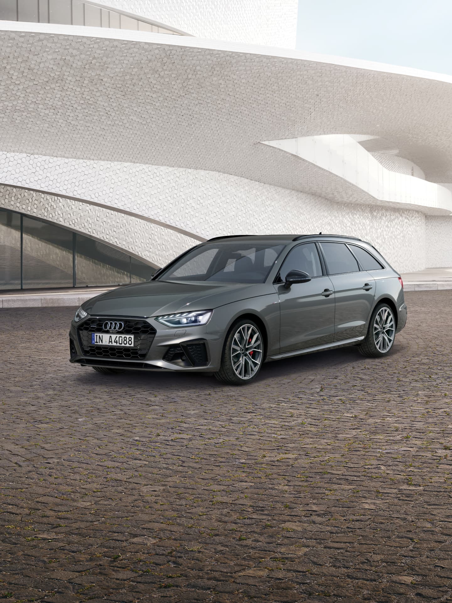 A grey car parked in front of a futuristic building with a textured facade.