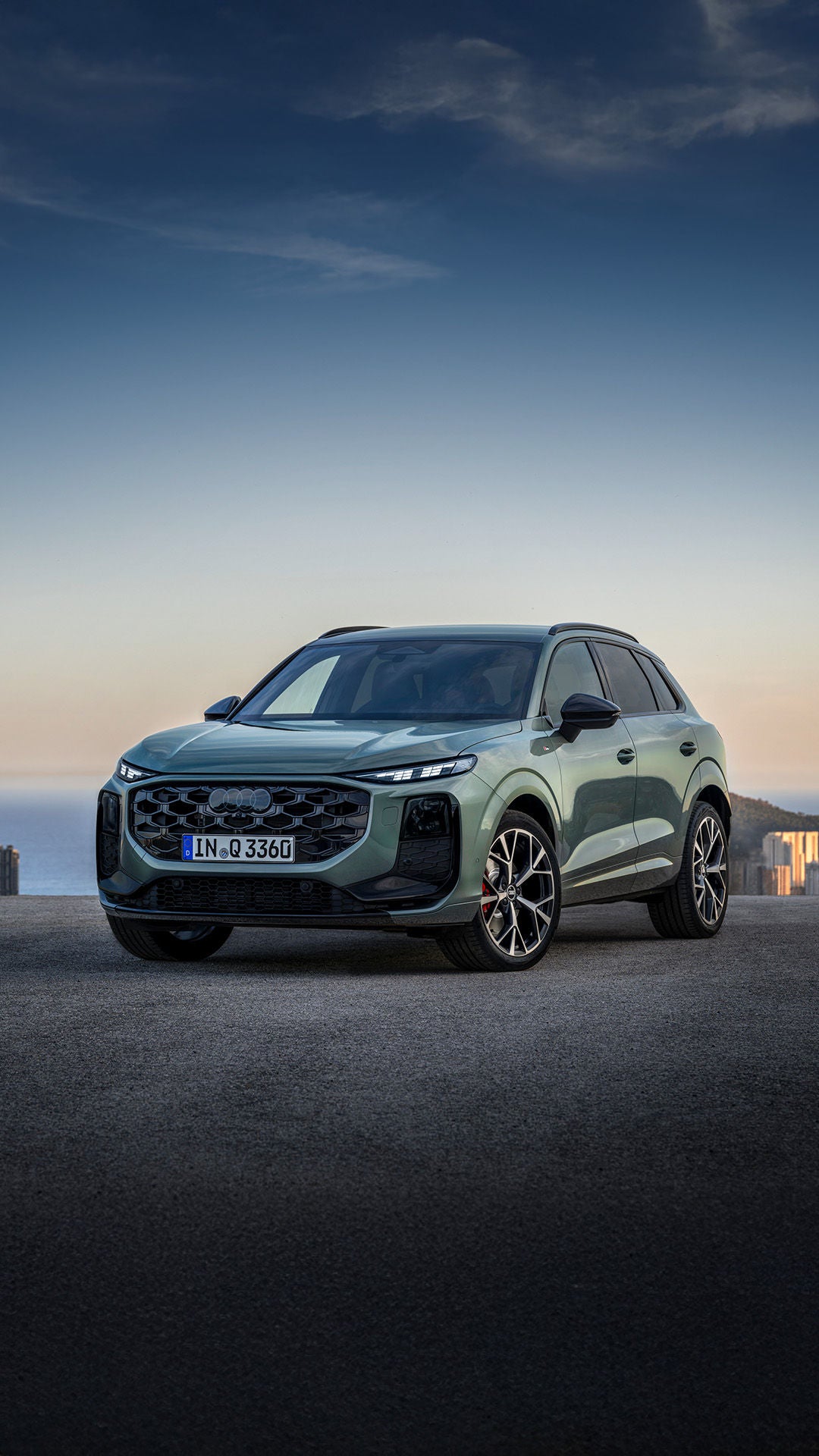 Dreiviertel Frontalansicht eines grünen Audi Q3 SUV auf einem Parkplatz vor urbaner Kulisse und mit Meer im Hintergrund.