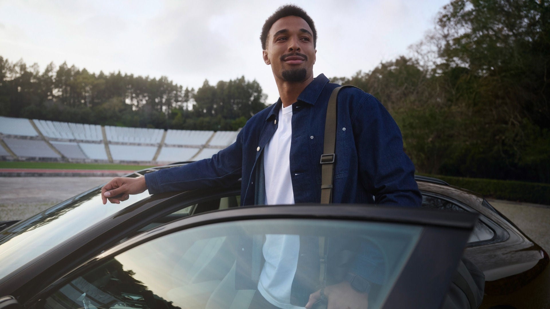 Leo Neugebauer steht in der geöffneten Fahrertür eines Audi A6 Avant, der in einem Stadion geparkt ist.