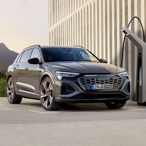 A black Audi SUV charging at a modern station with a mountain backdrop. The scene exudes elegance and innovation, highlighting electric mobility.