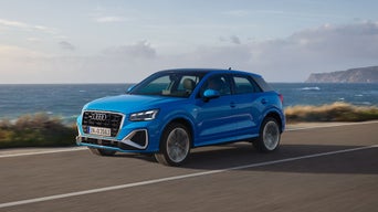 Blauer Audi Q2 fährt auf einer Küstenstraße, im Hintergrund das Meer und eine bewölkte Himmelskulisse.