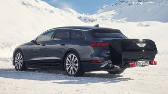 Dunkelblauer Audi mit Heckbox steht auf verschneiter Fläche vor Bergen.