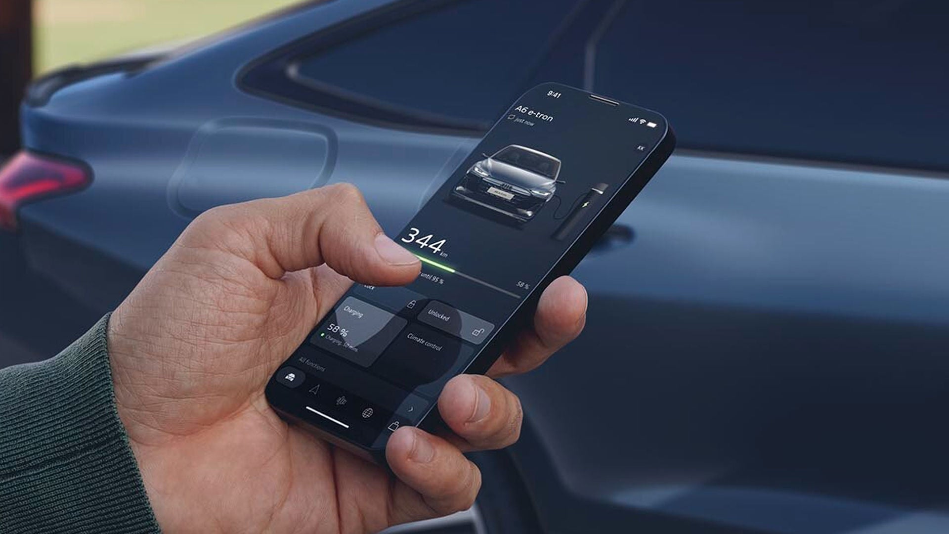 A person holding a smartphone displaying the myAudi app with an Audi vehicle blurred in the background.