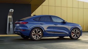 The SQ6 Sportback e-tron is parked sideways in a car park in front of a yellow façade and is connected to a charging station.