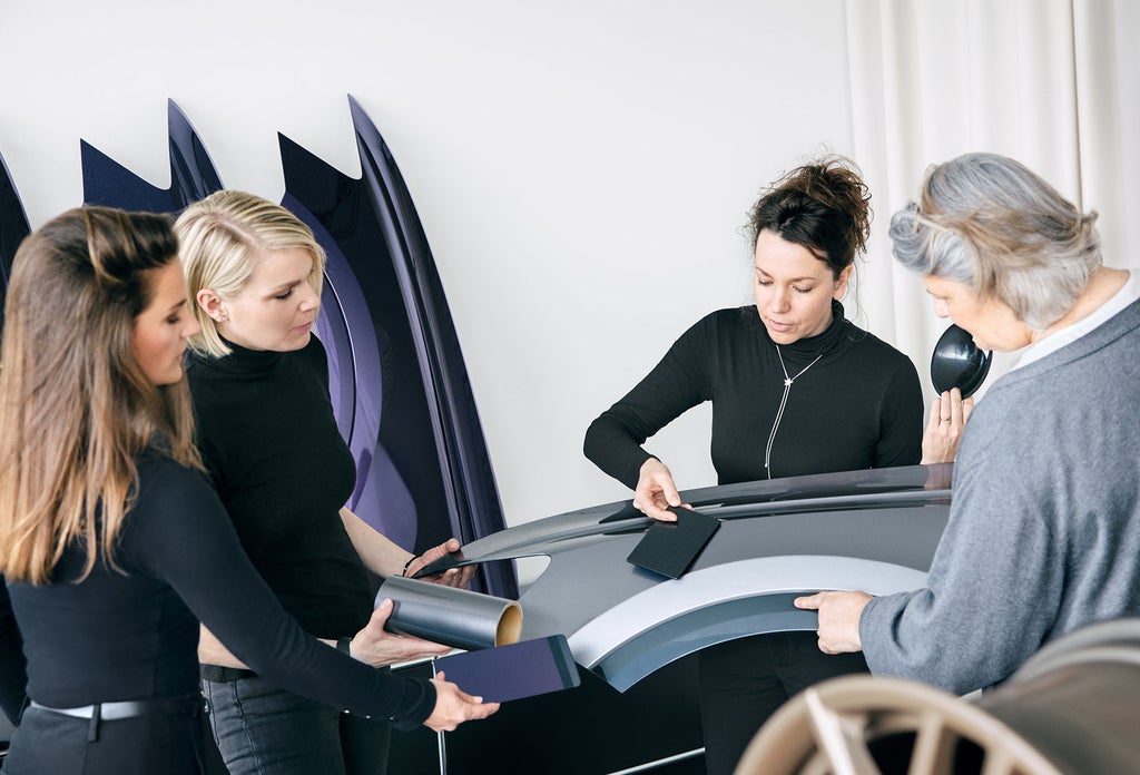 Das Color-&-Trim-Team hält Farb- und Materialproben an Karosserieteile