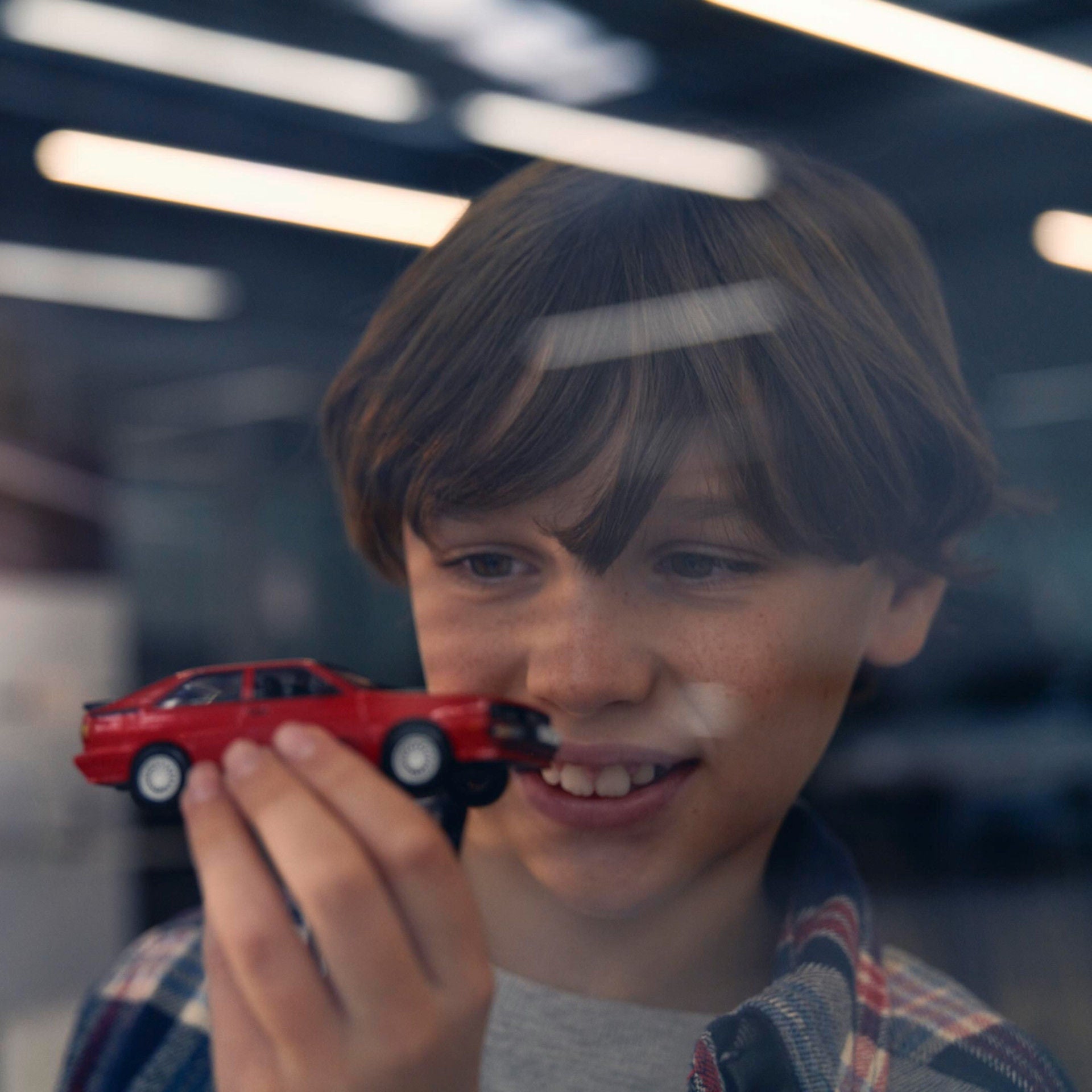Lächelnder Junge hält ein rotes Spielzeugauto vor einer beleuchteten Autohaus-Ausstellung