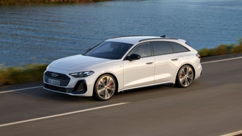 Weißer Audi A 5 fährt auf Küstenstraße entlang eines Gewässers.