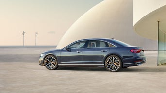 Ein grauer Audi A8 L steht seitlich vor moderner, heller Architektur bei Tageslicht.
