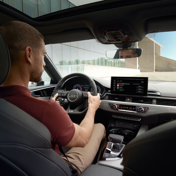 Driver's perspective inside an Audi, hands on steering wheel, dashboard visible.