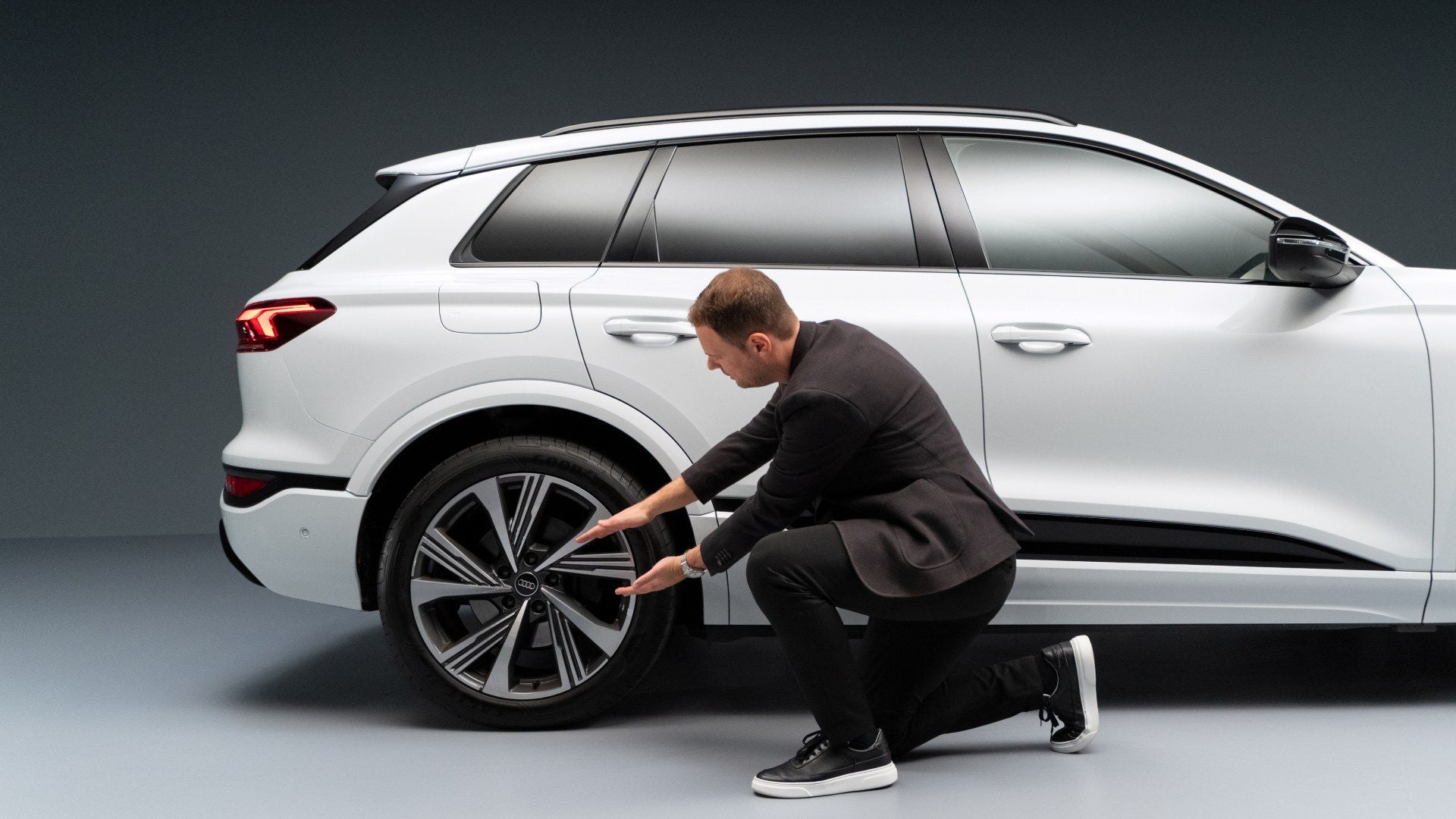 Andreas Ruf, systemteamleder hos Audi, på ett kne foran en Audi SQ6 SUV e-tron. Ruf holder begge hendene foran kjøretøyets dekk for å måle.  