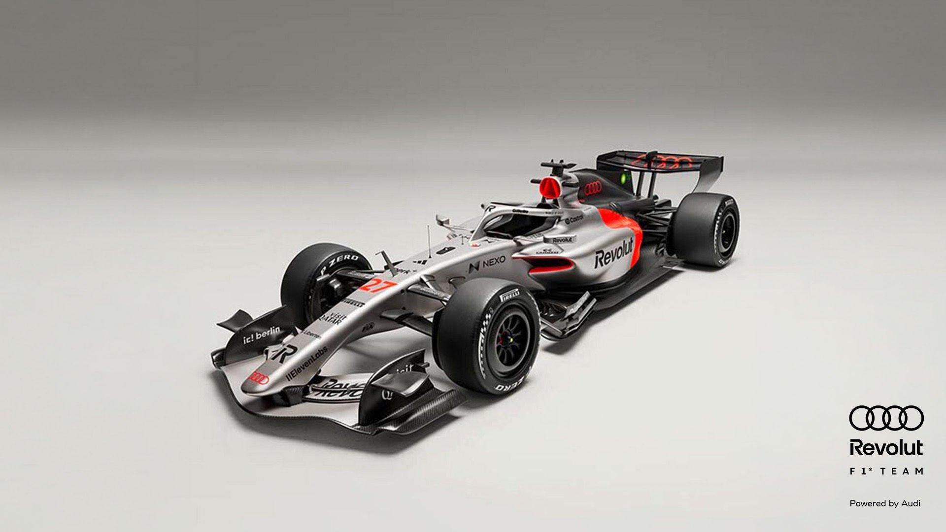 Schrägansicht eines silber-schwarzen Formel-1-Rennwagens mit roten Akzenten vor grauem Hintergrund, Audi- und Revolut-Logo in schwarz am Rand.