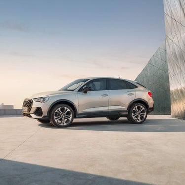 Full outdoor shot of a light beige Audi Q3 against a modern, geometrically patterned wall.