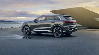 Side view of the Q5 SUV in anthracite in front of a modern building on the coast.