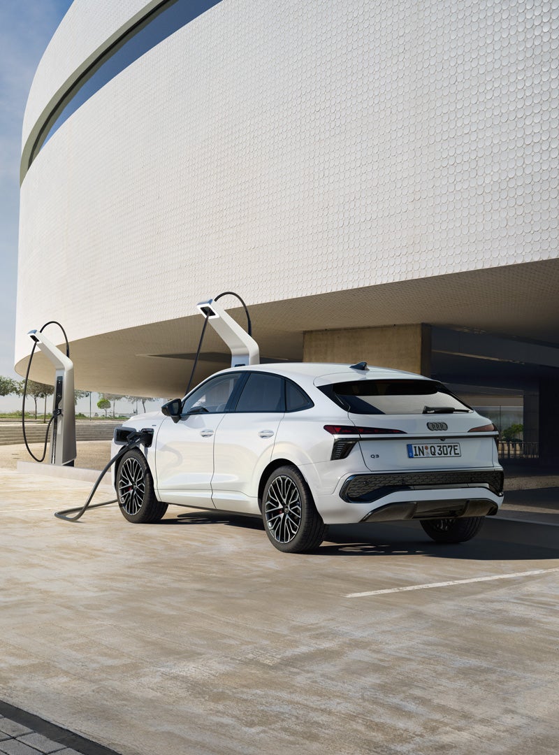 L’Audi Q3 Sportback e-hybrid è vista di profilo da dietro in una colonnina di ricarica pubblica in un parcheggio.