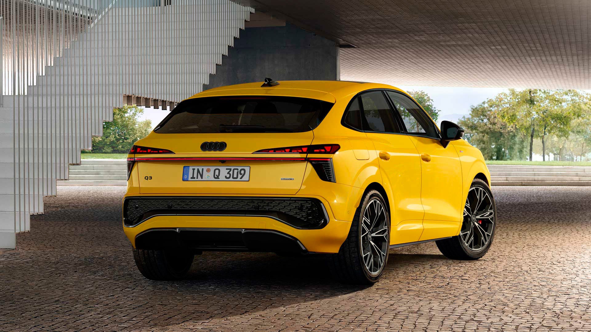 Un Q3 Sportback amarillo está aparcado en una superficie pavimentada delante de la barandilla de una escalera.