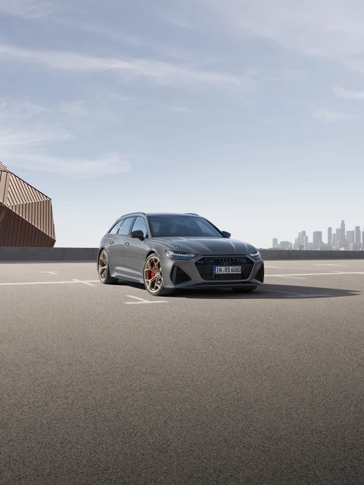 A grey car parked on an empty lot with a city skyline in the background.