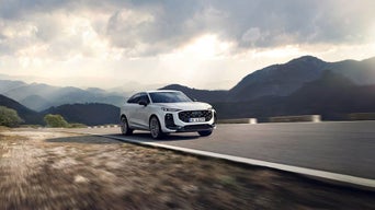 Weißer Audi SUV fährt auf Bergstraße bei Sonnenuntergang.