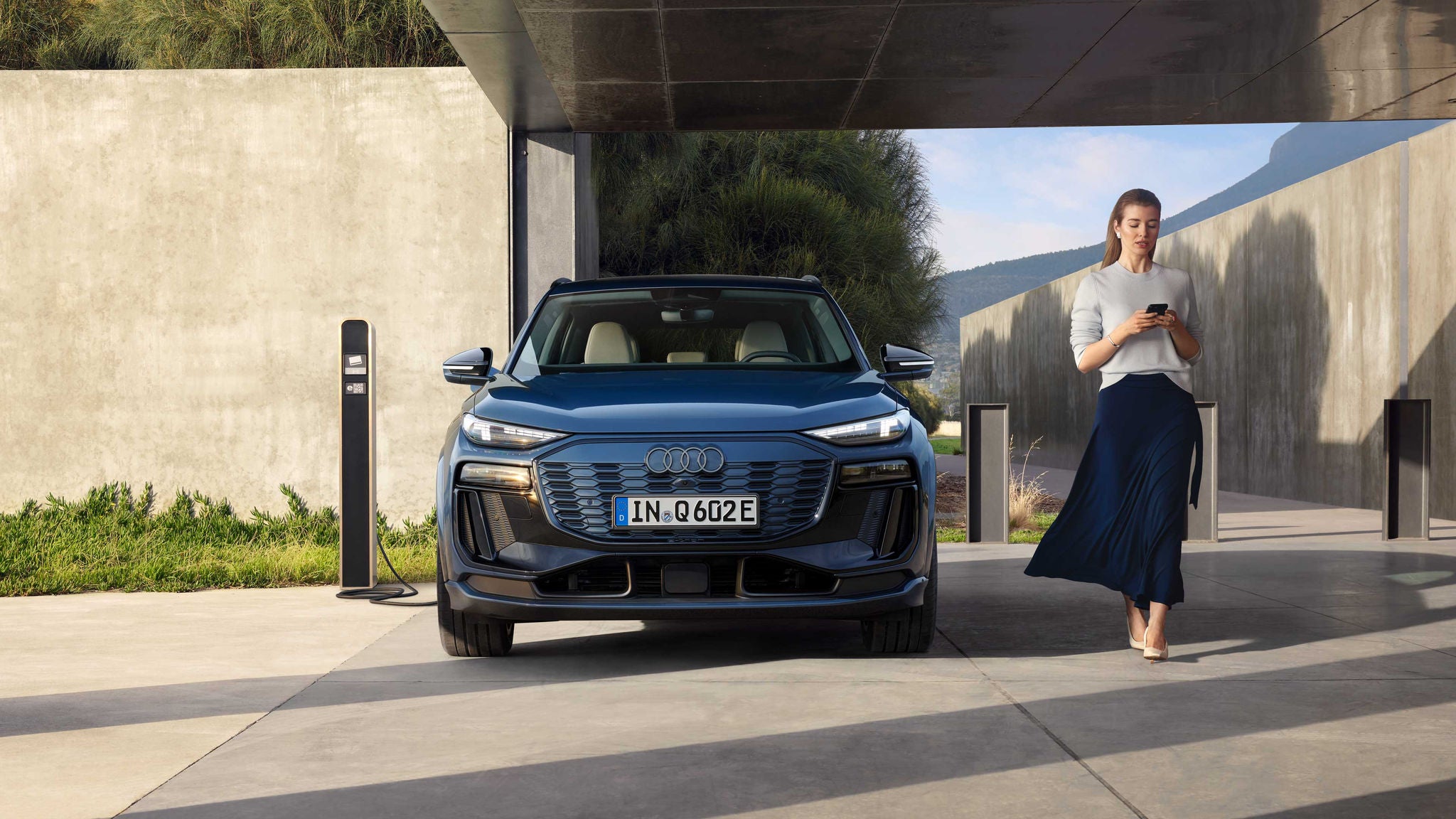 Eine Frau geht an einem geparkten Audi Q6 e-tron vorbei, der an einer Ladesäule angeschlossen ist.