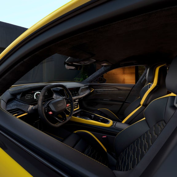 Innenraum eines gelben Audi RS e-tron GT performance mit schwarzem Leder, gelben Akzenten und digitalem Cockpit, aufgenommen durch die offene Tür.